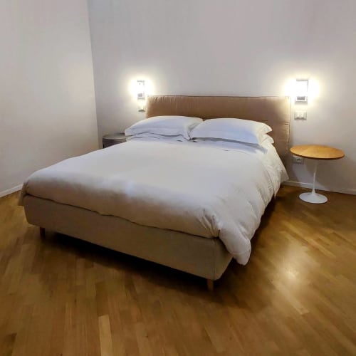 Modern bedroom at Stella CasaBono hotel in Sulmona with tan upholstered bed, white linens, wall sconces, and wooden floors