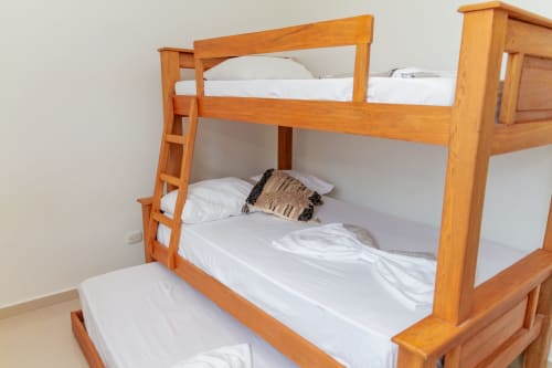 Cama litera de madera con ropa blanca y almohada decorativa en el hotel Olamar Living de Coveñas, Sucre, Colombia