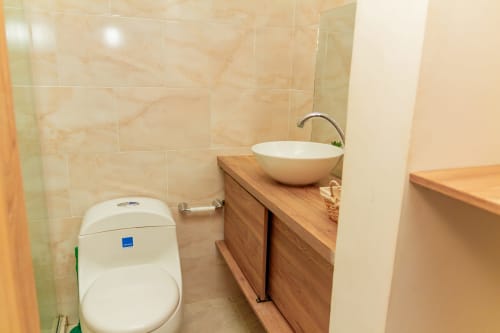 Moderno baño en Olamar Living con lavamanos blanco sobre vanidad de madera, inodoro y paredes revestidas en cerámica beige en Santiago de Tolú