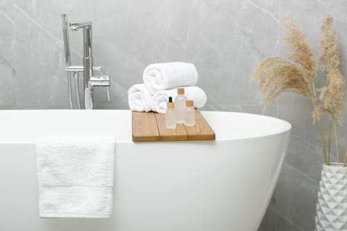 Salle de bain moderne à Vista D'oro avec baignoire blanche, serviettes roulées, accessoires de bain sur plateau en bois et décor de pampa