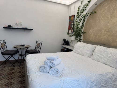 Quarto moderno da B&B I MORI em Catânia com cama branca, toalhas enroladas, área de estar e plantas suspensas acima da cabeceira