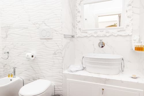 Banheiro moderno e branco no B&B I MORI Catania com azulejos de mármore, lavatório tipo cuba, vaso sanitário, espelho e artigos de higiene