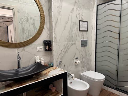 Bagno moderno del B&B I MORI Catania con pareti in marmo, lavabo nero, water, bidet e box doccia in vetro