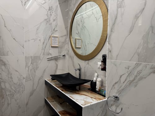 Bagno moderno del B&B I MORI Catania con pareti in marmo, lavabo nero, specchio rotondo con cornice dorata e vanity in marmo