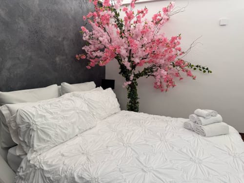 Camera moderna del B&B I MORI Catania con letto bianco, albero in fiore rosa e parete grigia di accento