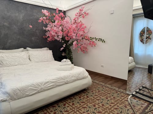 Elegante camera presso B&B I MORI Catania con letto bianco, composizione floreale rosa, parete d'accento scura e balcone con vista sulla città