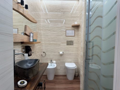 Baño moderno en B&B I MORI Catania con lavabo negro, inodoro blanco, estantería de madera y ducha con mampara de vidrio