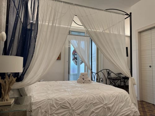 Elegante letto a baldacchino con biancheria bianca e tende trasparenti nella camera Gli Amanti del B&B I MORI, Catania, con vista sul balcone