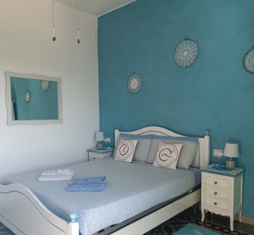 Turquoise bedroom at B&B Eleonora D'Arborea in Posada with queen bed, white nightstands, and sea view wall decorations