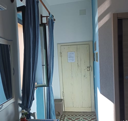 Azzurra Room at B&B Eleonora D'Arborea in Posada showing blue curtains, pale yellow door, and bright natural light from