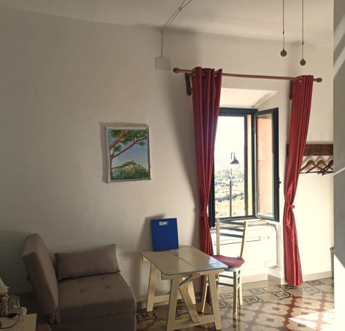 Bright bedroom at B&B Eleonora D'Arborea in Posada with gray sofa, small table, burgundy curtains framing glass door to