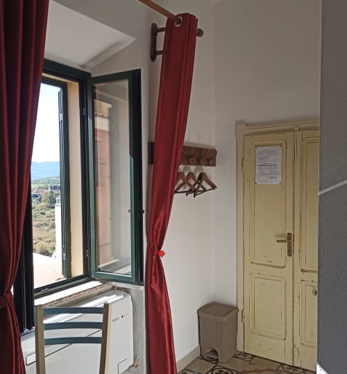 Sarda Room at B&B Eleonora D'Arborea in Posada with open window, red curtains, wooden hangers, and city view balcony access