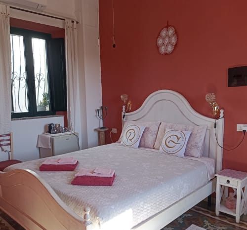Eleonora Room at B&B Eleonora D'Arborea in Posada with white bed, red walls, and city views from black-framed window