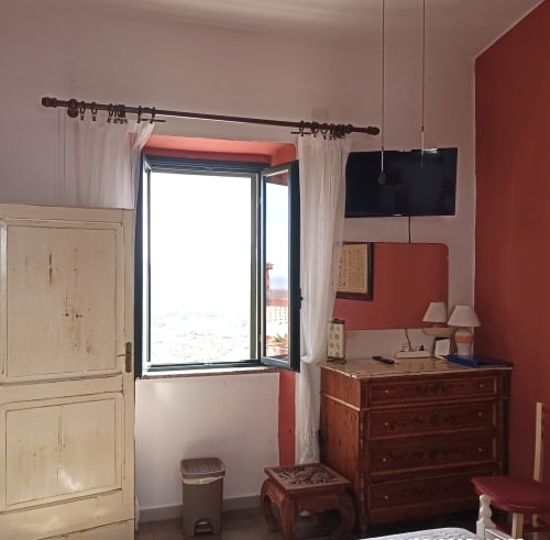 Eleonora Room at B&B Eleonora D'Arborea in Posada with city view, flat-screen TV, wooden dresser, and open window with sheer