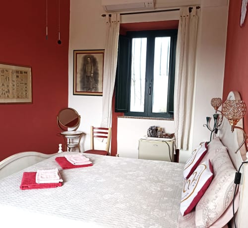 Bright bedroom at B&B Eleonora D'Arborea in Posada with red walls, white bed, and French doors opening to balcony