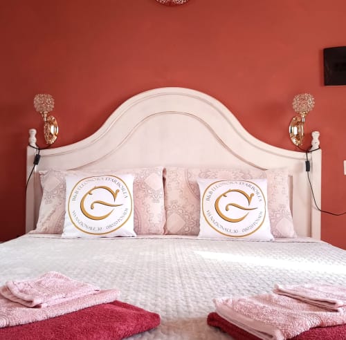 Elegant bedroom at B&B Eleonora D'Arborea in Posada with coral walls, white headboard, and pink bedding with hotel logo