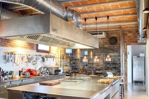 Modern industrial kitchen at Finques Garcia Enrich in Palafrugell with stainless steel counters, exposed brick, and wooden