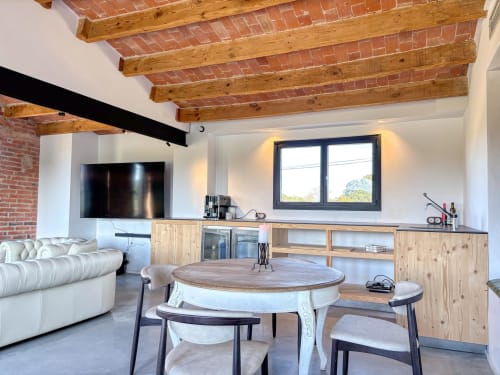 Modern loft-style living room at Finques Garcia Enrich with exposed brick, wooden beams, round dining table, and