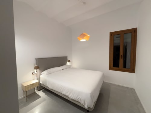 Modern bedroom at Finques Garcia Enrich in Palafrugell with white bedding, gray headboard, wooden nightstand, and pendant