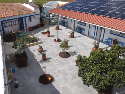 Casa do Pão courtyard in Campinho with paved terrace, potted plants, solar panels, and blue-trimmed buildings.