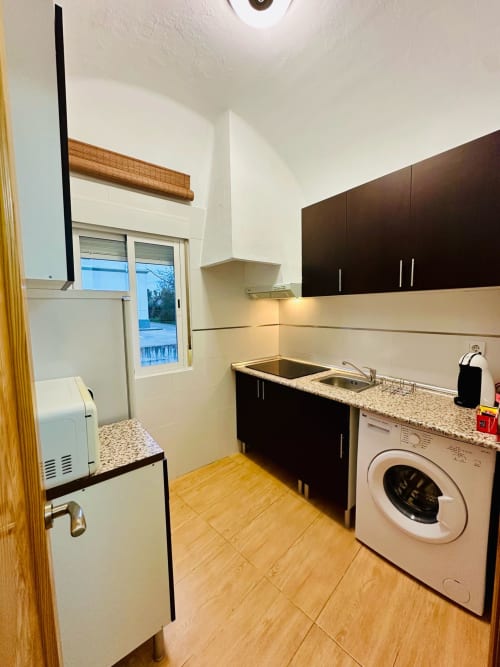 Cocina moderna en apartamento de Mérida con muebles negros, encimeras de granito, lavadora y vistas a la ciudad