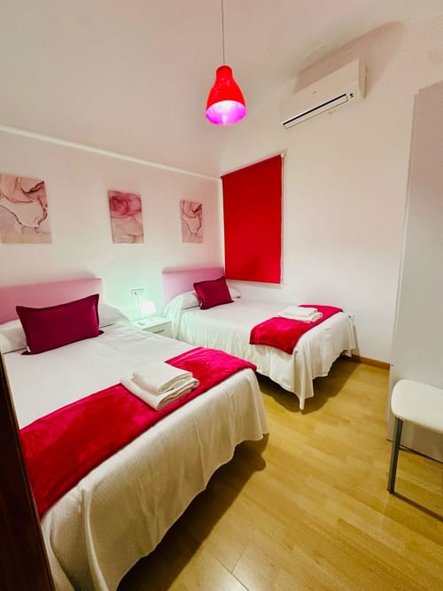 Moderna habitación doble en apartamento Gestyp-AT en Mérida con acentos rojos, ropa de cama blanca y lámpara colgante rosa