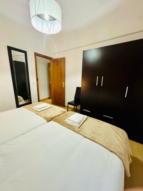 Moderno dormitorio en Mérida con camas gemelas, armario negro, espejo e iluminación colgante contemporánea