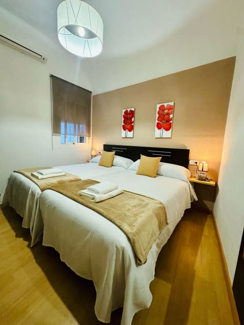 Dormitorio moderno con camas gemelas, cabecera negra, detalles amarillos y cuadro de flores rojas en el apartamento Gestyp-AT de Mérida