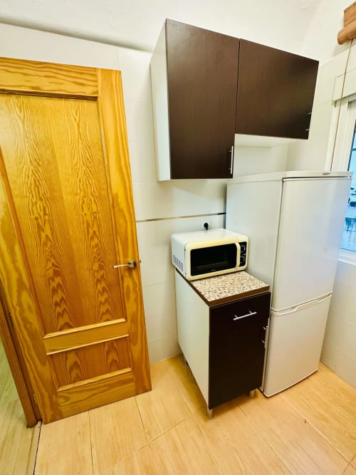 Área de cocina compacta en apartamento de Mérida con microondas, refrigerador, muebles de madera y gabinetes superiores oscuros