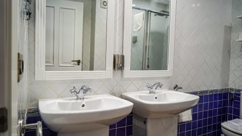 Baño con doble lavabo de pedestal blanco, detalles en azulejos azules y botiquines con espejo en apartamento Gestyp-AT, Mérida