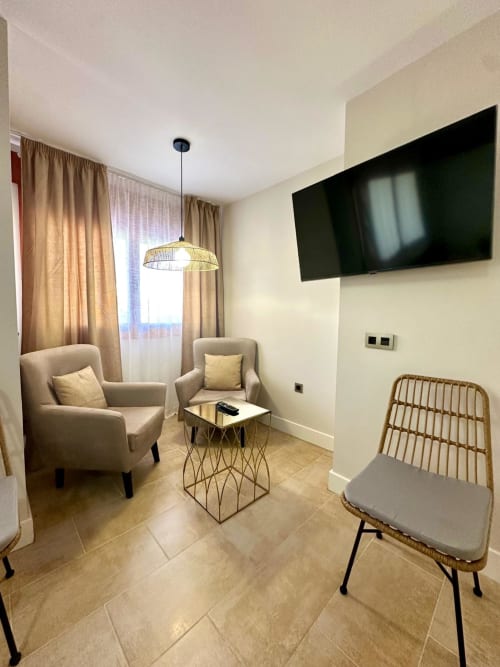 Moderno salón en Mérida con sillones beige, TV de pared, lámpara colgante y vistas a la ciudad