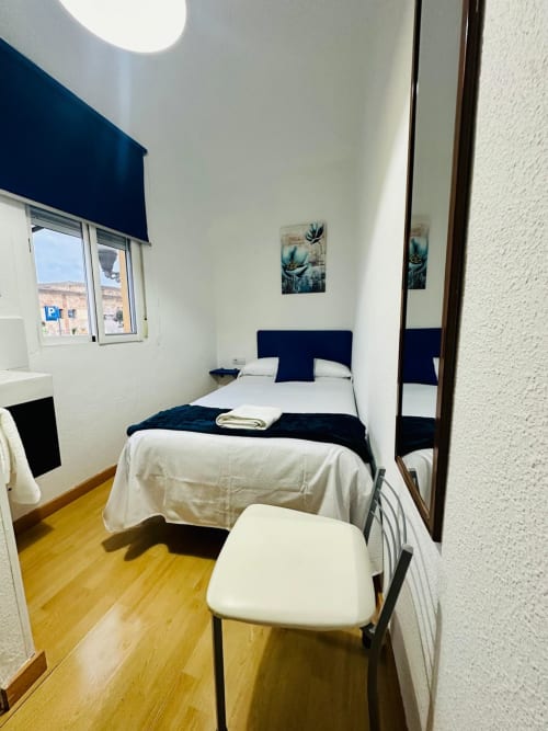 Moderno dormitorio de apartamento en Mérida con vista a la ciudad, cabecero azul marino, ropa de cama blanca, piso de madera y persiana azul