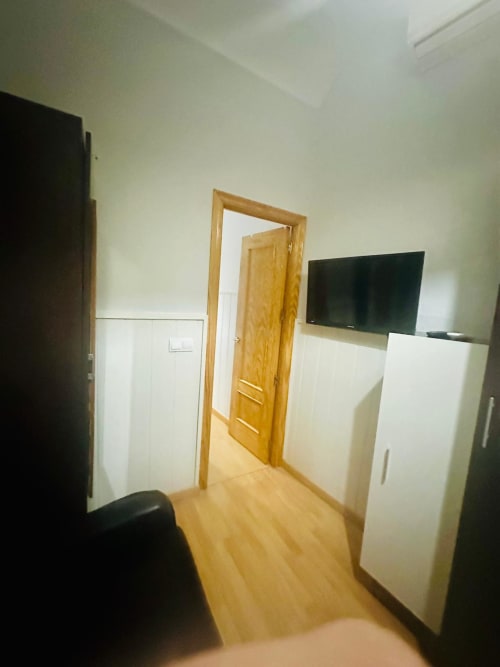 Moderno dormitorio de apartamento en Mérida con puerta de madera, armario blanco, TV montado y piso de madera