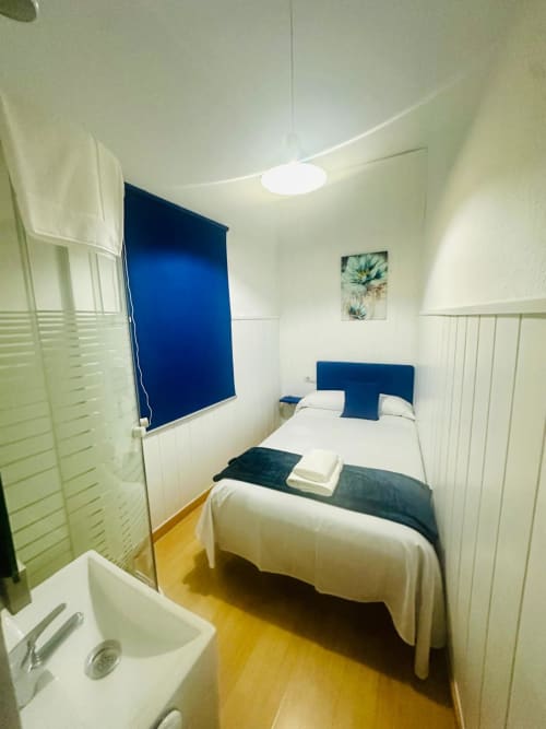 Dormitorio acogedor con cabecera azul y ropa de cama blanca en apartamento de Mérida, piso amarillo, lámpara de escritorio