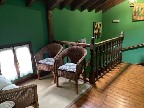 Dormitorio verde en Casa La Huerta con sillas de mimbre, vigas de madera y barandilla con vistas a Cangas de Onís
