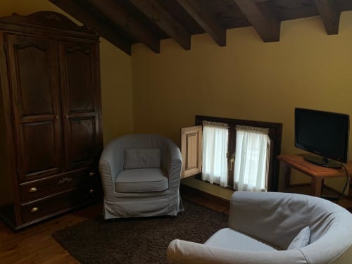 Acogedora sala de estar en Casa La Huerta con cómodos asientos, vigas oscuras y vistas al jardín en Cangas de Onís