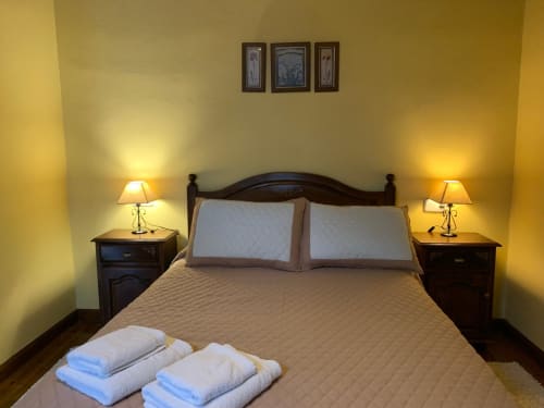 Acogedora habitación de Casa La Huerta con paredes amarillo cálido, cama de madera oscura, lámparas de noche y vistas al jardín cerca de Cangas de