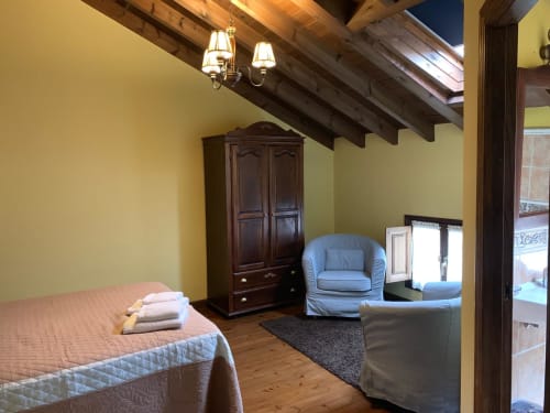Acogedora habitación en Casa La Huerta con paredes amarillas, vigas de madera, sillón azul y vistas al jardín en Cangas de Onís