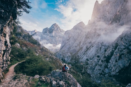 Senderista con mochila en sendero de montaña con vistas a espectaculares picos de piedra caliza y valle cerca de Cangas de Onís