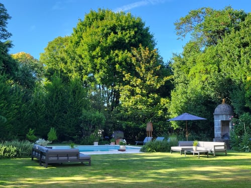 Jardin du Logis des Tourelles avec piscine, transats, parasol bleu et arbres luxuriants à Cognac