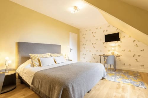 Helles Dachzimmer im Gästehaus Les logis de Kergoulou in Concarneau mit gelben Wänden, grauem Bett und Holzböden