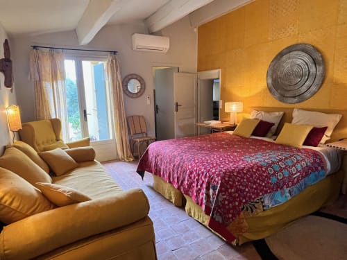 Warm golden bedroom at Saint Martin B&B in Ollioules with mustard chair, patterned bedding, and terracotta accent wall