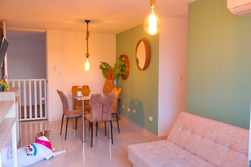 Habitación triple moderna en Olamar Living, Coveñas, con sofá rosa, zona de comedor, iluminación colgante y pared de acento verde