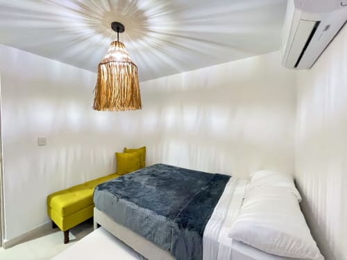 Moderna habitación en Olamar Living con cama queen, sillón amarillo, lámpara colgante de latón y paredes blancas en Coveñas, Colombia