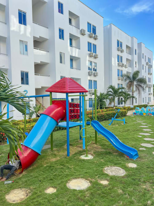 Parque infantil colorido con tobogán rojo y azul en frondoso jardín del hotel Olamar Living, Coveñas, Colombia