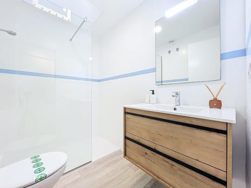 Baño moderno de la casa rural Mar Blau de Estartit Rental con tocador de madera, azulejos blancos y franja de acentos azules