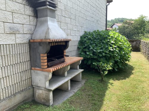 Barbacoa de ladrillo al aire libre en Casa La Huerta, Cangas de Onís, rodeada de exuberante jardín y muros de piedra