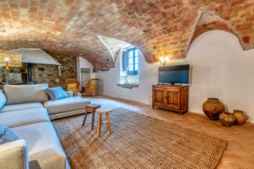 Salon rustique avec plafond voûté en brique, canapé gris, meuble télé en bois et poterie terracotta aux Finques Garcia Enrich