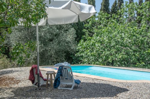 Zone de détente au bord de la piscine de Finques Garcia Enrich avec parasol, chaise longue et piscine bleu vif entourée de verdure