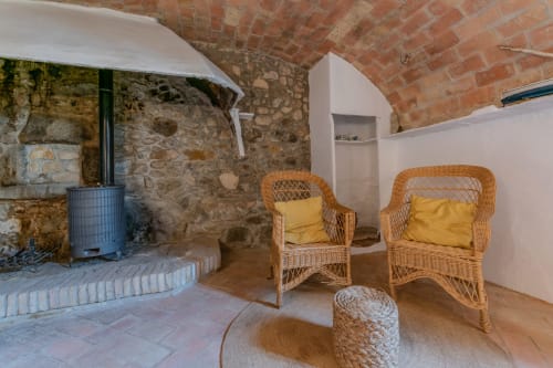 Chambre rustique en pierre avec chaises en osier, coussins jaunes et poêle à bois à Finques Garcia Enrich, Palafrugell